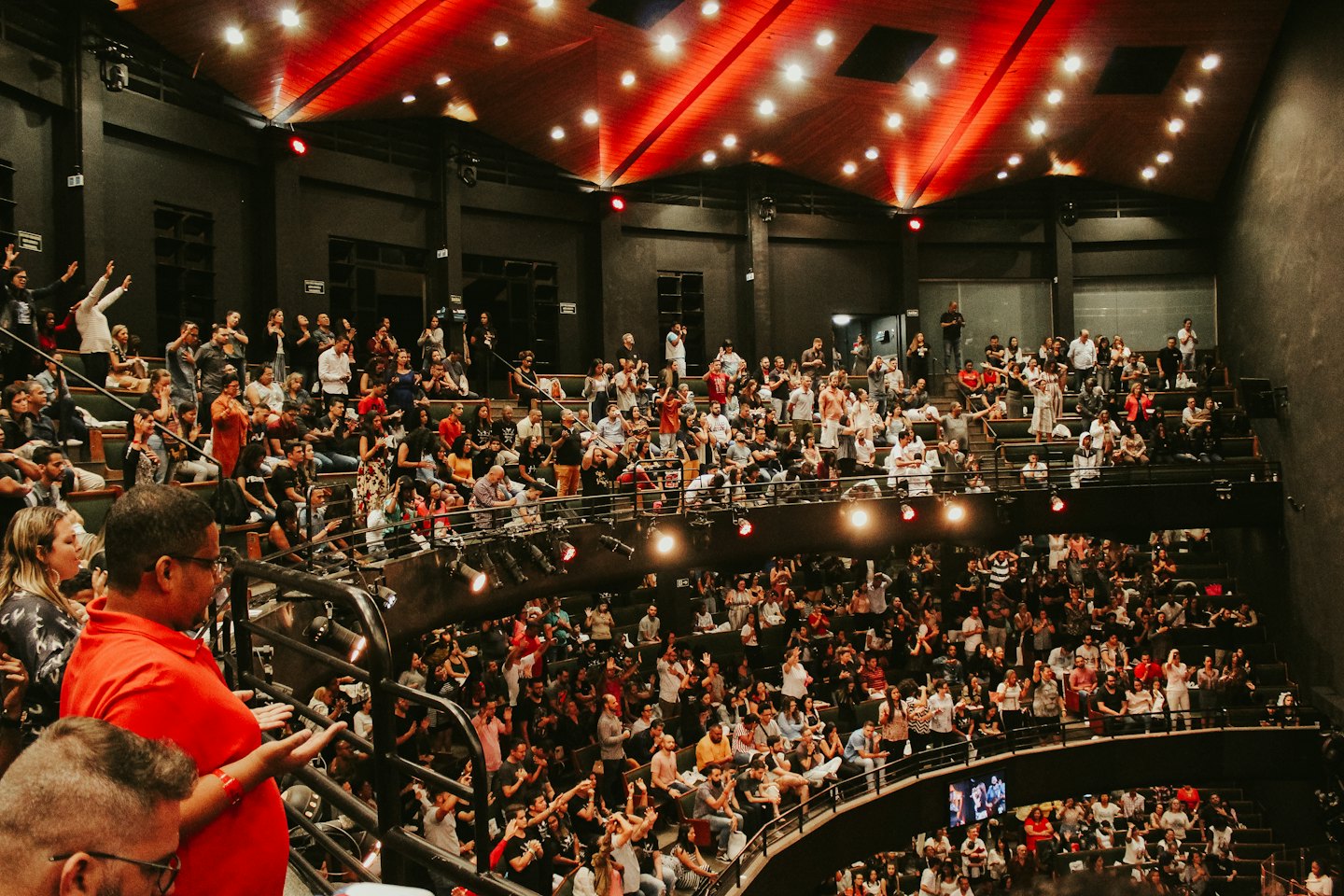An enthusiastic audience stands and applauds inside a large auditorium.