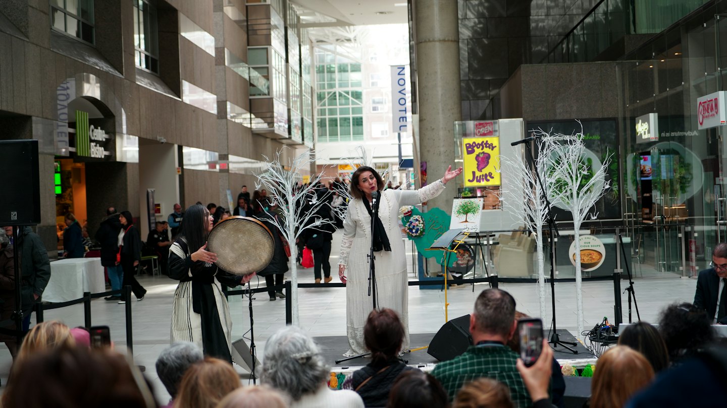 Two performers sing and play a drum on a stage.